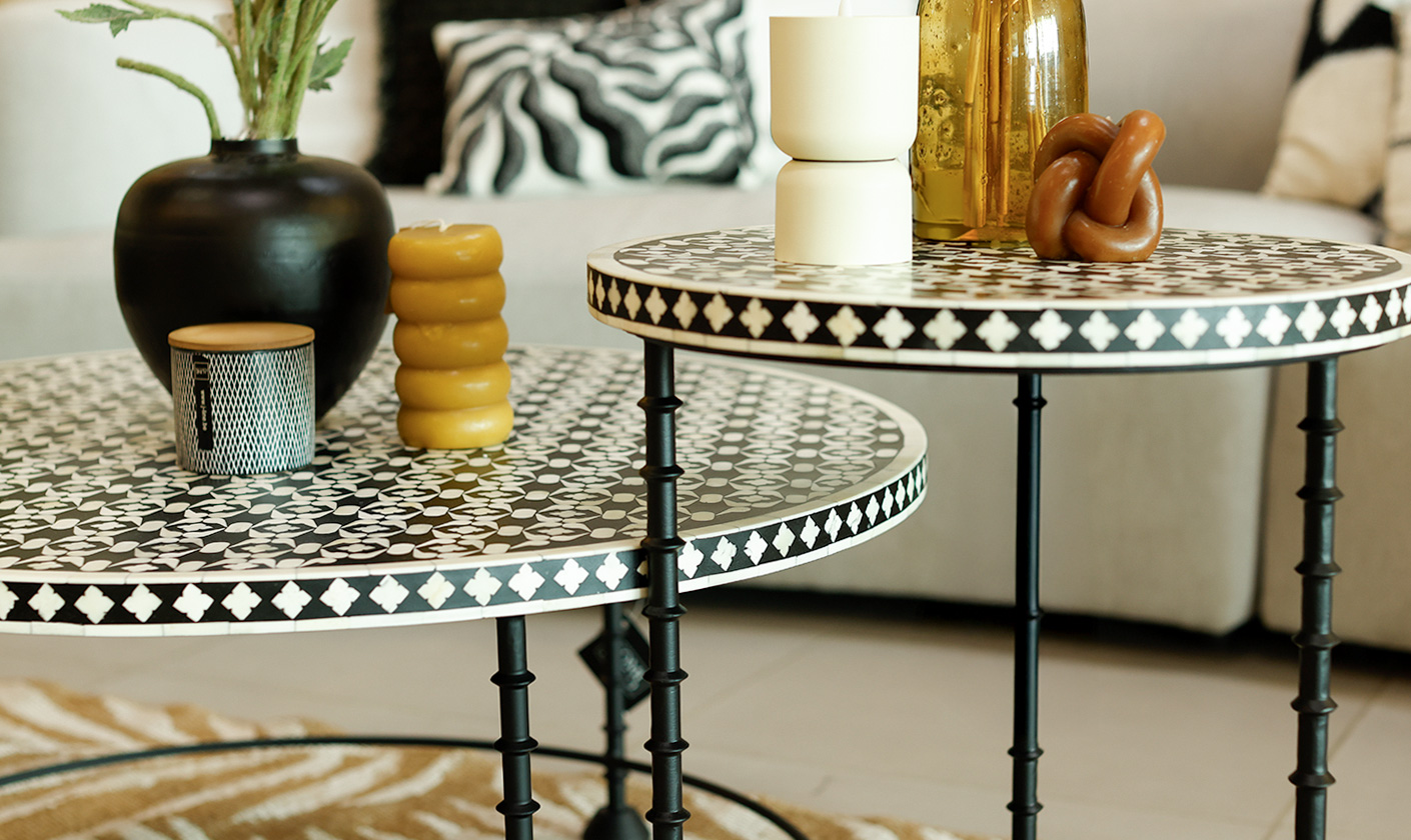 Pair of round patterned side tables with black legs, styled with decorative candles, vases, and modern accents in a living room setting.